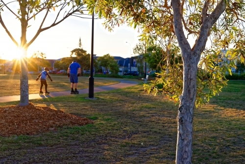 Father and son roller skating at a park at sunset with sunflare, golden hour - Australian Stock Image