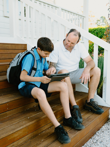 Father and son sitting on the steps using an iPad. - Australian Stock Image