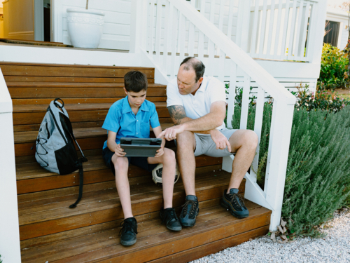 Father and son sitting on the steps using an iPad. - Australian Stock Image
