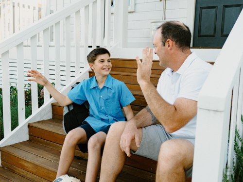 Father and son sitting on the wooden steps of their porch. - Australian Stock Image