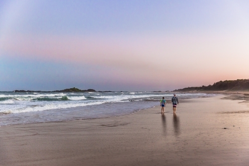 Father and son walking on beach at sunset from behind - Australian Stock Image