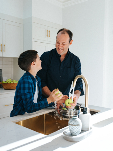 Father and son washing apples in the kitchen sink. - Australian Stock Image