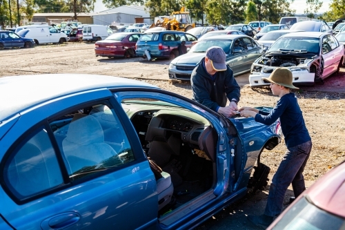 Father and son working a wreckers pulling apart old car for parts - Australian Stock Image