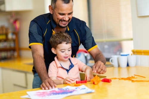Father and toddler son playing with coloured dough in kitchen - Australian Stock Image