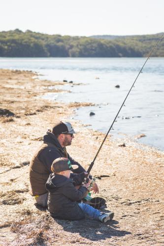 Father and young boy together fishing on the banks of a river