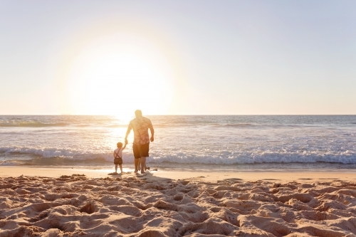 Father And Young Child Holding Hands On The Beach At Sunset