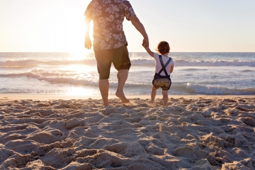 Father And Young Child Holding Hands On The Beach At Sunset - Australian Stock Image