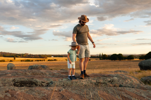 Father and young daughter on adventure over rocks through grassy paddock at sunset - Australian Stock Image