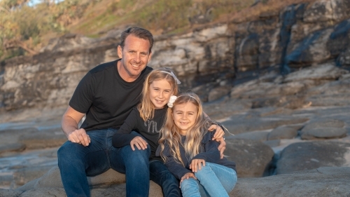 Father and young daughters sitting on a large boulder - Australian Stock Image