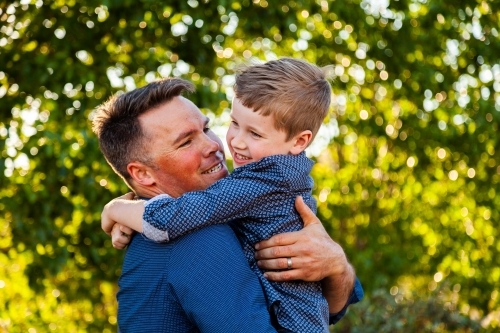 Father and young son laugh together and hug outside - Australian Stock Image