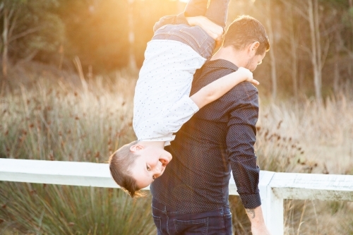 Father being silly with child holding son upside down over shoulder