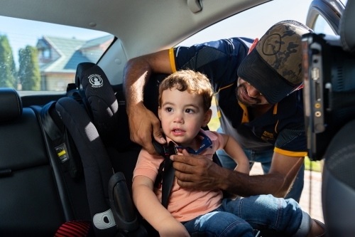 father buckling child into car seat restraint - Australian Stock Image