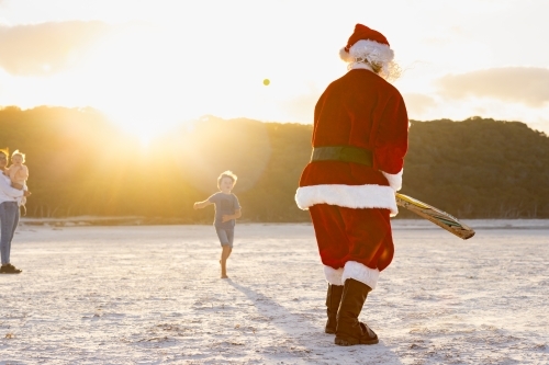 father christmas seen from behind facing a loose ball in beach cricket - Australian Stock Image