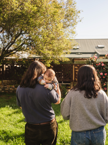 Father cradles baby over his shoulder with mum behind - Australian Stock Image