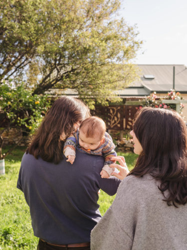 Father cradles baby over his shoulder with mum behind - Australian Stock Image