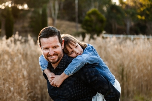 Father giving child a piggy back ride while she hugs him - Australian Stock Image