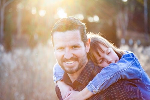 Father giving child a piggy back ride while she hugs him - Australian Stock Image