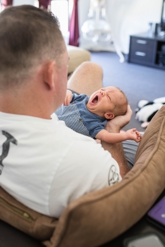 Father holding newborn baby boy stretching and yawning - Australian Stock Image