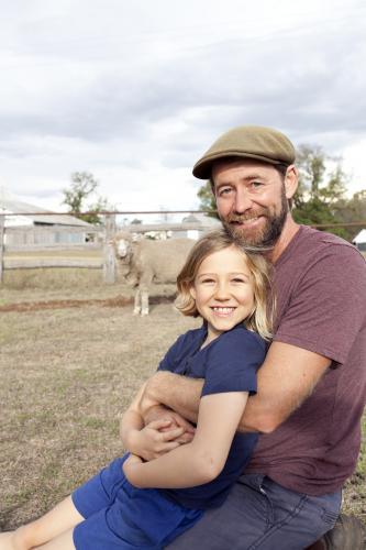Father hugging daughter on farm with sheep in background - Australian Stock Image