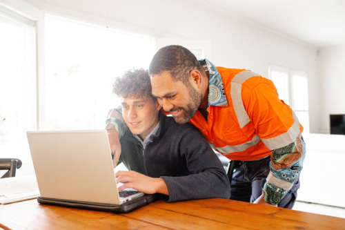 Father in high vis clothing helping teenage son with homework in a laptop - Australian Stock Image
