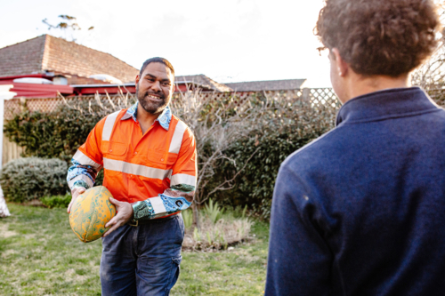 Father in high vis clothing playing with ruby ball with teenage son in the garden - Australian Stock Image