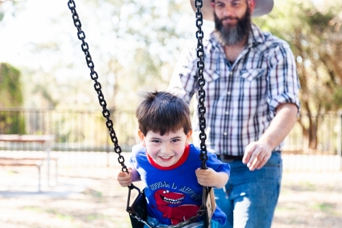 Father pushing son on the swing at the park - Australian Stock Image