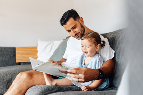 Father reading story with toddler daughter on the couch - Australian Stock Image