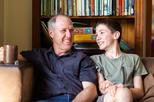 Father sitting with son on lounge drinking coffee - Australian Stock Image
