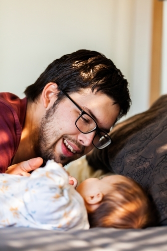 Father smiling and interacting with baby in morning sunlight on bed