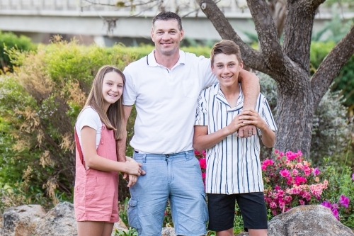 Father standing with arm around son while daughter cuddles into arm - Australian Stock Image