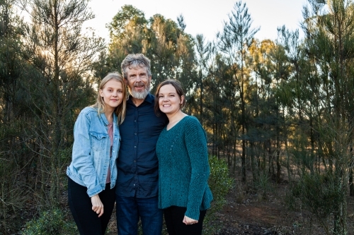 Father standing with happy daughters outside in bushland - Australian Stock Image