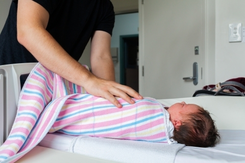 Father wrapping up day old newborn baby in hospital blanket - Australian Stock Image