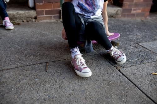 Feet and legs of a girl sitting on skateboard on footpath - Australian Stock Image