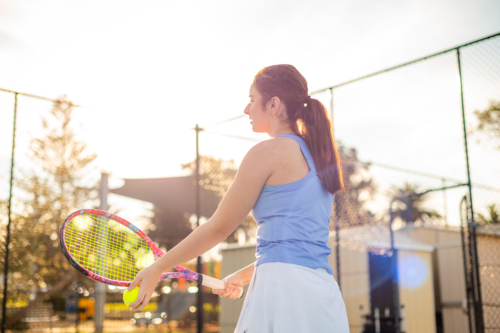 Female athlete prepares to serve tennis ball on outdoor court under sunny sky - Australian Stock Image