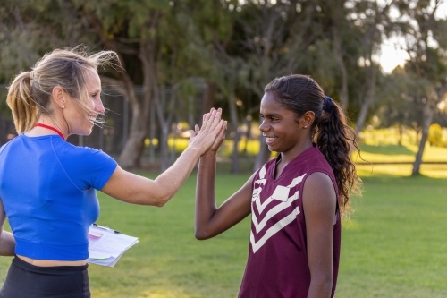 female coach high fives aboriginal student football player - Australian Stock Image