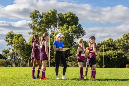 female coach holding clipboard addressing schoolchildren in sports uniforms - Australian Stock Image