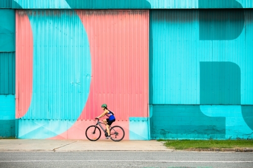 Female Cyclist Riding by a Colourful Wall - Australian Stock Image