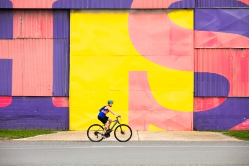 Female Cyclist Riding by a Colourful Wall - Australian Stock Image