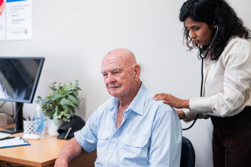 Female doctor listens to elderly mans back using a stethoscope during a routine check‑up - Australian Stock Image