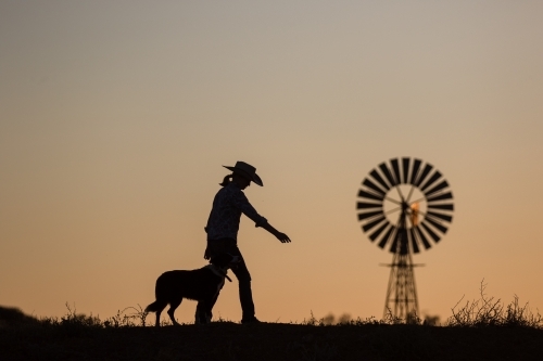 Female farmer, dog and windmill in silhouette - Australian Stock Image