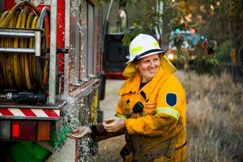 Female firefighter laughing and washing her hands beside firetruck - Australian Stock Image