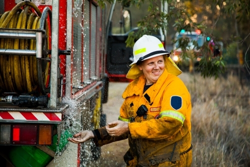 Female firefighter laughing and washing her hands beside firetruck