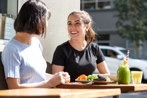 Female friends sitting outdoors at cafe in sunshine - Australian Stock Image