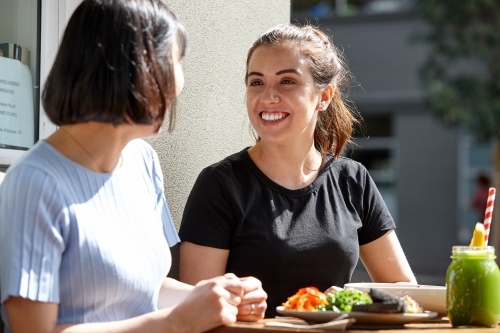 Female friends sitting outdoors at cafe in sunshine - Australian Stock Image