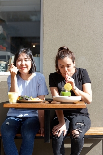 Female friends sitting outdoors at cafe in sunshine - Australian Stock Image