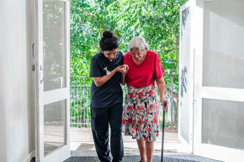 Female health caregiver assisting an elderly woman walking through the doorway - Australian Stock Image