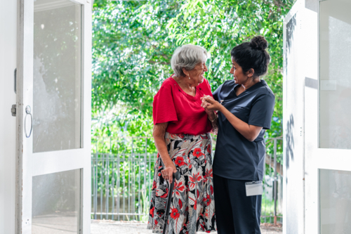 Female health caregiver assisting an elderly woman walking through the doorway - Australian Stock Image