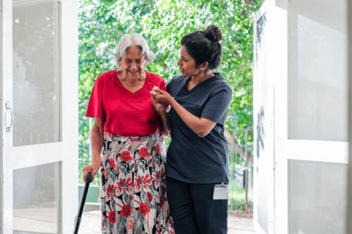 Female health caregiver assisting an elderly woman walking through the doorway - Australian Stock Image