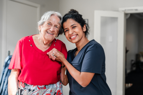 Female health caregiver assisting an elderly woman walking through the doorway - Australian Stock Image