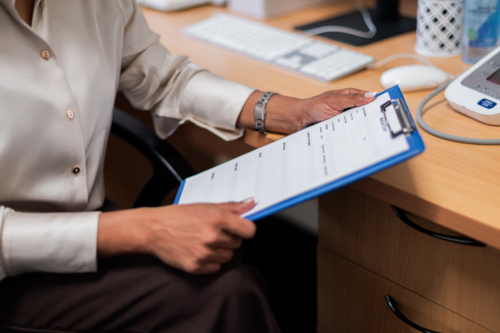 Female healthcare practitioner looking at the form on a clipboard while seated behind the desk - Australian Stock Image